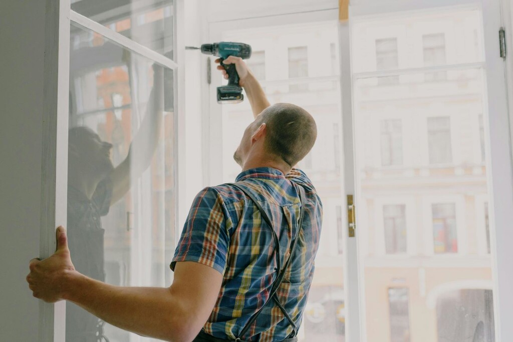 A handyman is installing a window frame with a drill