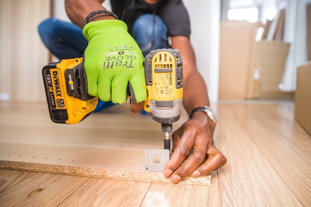 A person using Dewalt cordless impact driver on brown board.