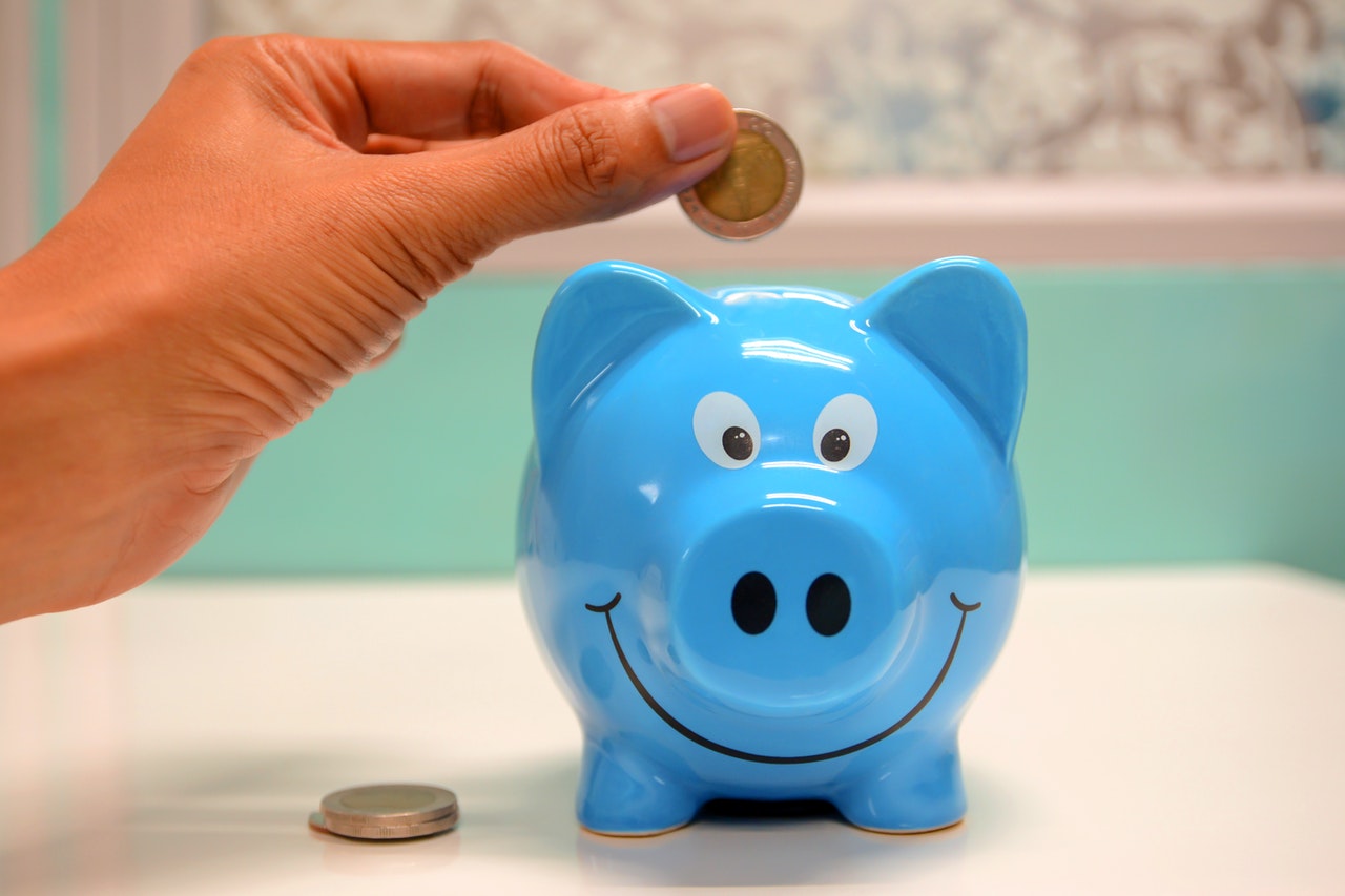 A person putting a coin in a blue piggy bank.